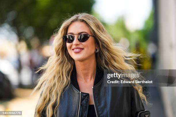 Emili Sindlev wears black sunglasses, a black shiny leather oversized bomber coat from Prada, a black shoulder-off cropped top, outside the Prada...
