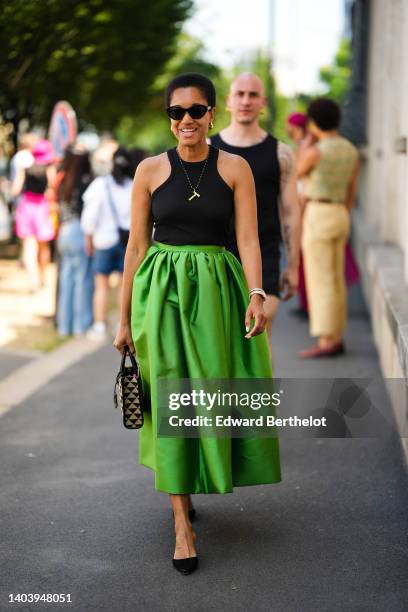 Tamu McPherson wears black sunglasses, gold earrings, a black / red / yellow / green pearls long necklace with a wood pendant, a black halter-neck...