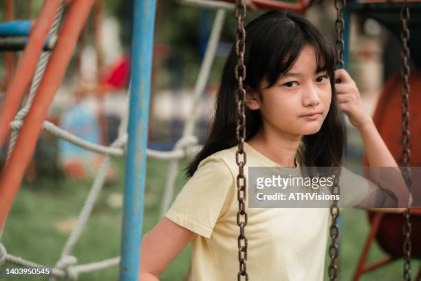 porträt traurig child tween mädchen sitzt auf der schaukel auf dem spielplatz und schaut in die kamera. störend - thai ethnicity stock-fotos und bilder