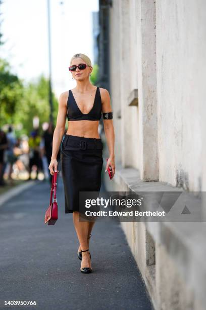 Caroline Daur wears burgundy sunglasses, silver and black triangle pendant earrings from Prada, a black V-neck satin cropped top from Prada, a...
