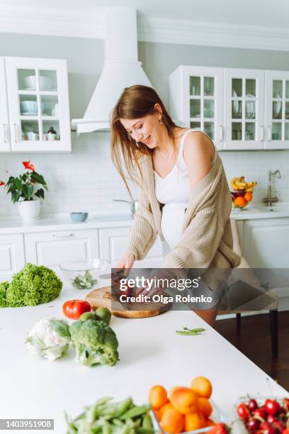 middle age beautiful pregnant woman preparing healthy meal with green vegetables at home - chopping vegetables stock pictures, royalty-free photos & images