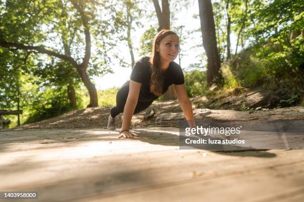woman doing push-ups outside in a public park - opdrukken stockfoto's en -beelden