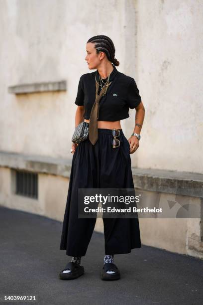 Guest wears silver and gold chain necklaces, a black short sleeves / cropped polo shirt from Lacoste, a brown with pink and black striped print...