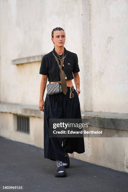 Guest wears silver and gold chain necklaces, a black short sleeves / cropped polo shirt from Lacoste, a brown with pink and black striped print...