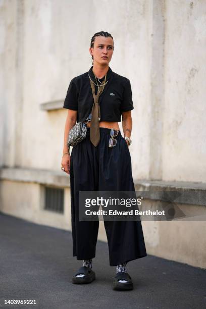 Guest wears silver and gold chain necklaces, a black short sleeves / cropped polo shirt from Lacoste, a brown with pink and black striped print...