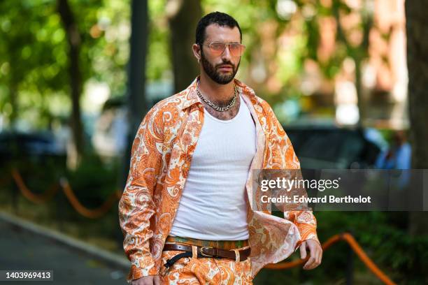 Guest wears orange sunglasses, a large chain necklace, a white ribbed tank-top, a white with orange print pattern shirt from Etro, a dark brown shiny...