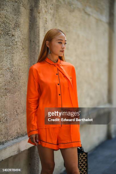 Guest wears a black and silver triangle pendant earrings from PRada, a neon orange oversized silk shirt from Prada, matching neon orange silk shirt...