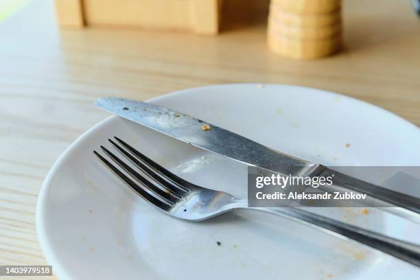 a dirty plate, fork and knife on a wooden dining table, in a cafe, at home or in a restaurant. used cutlery symbolizes the end of lunch or dinner. - cleaning after party - fotografias e filmes do acervo