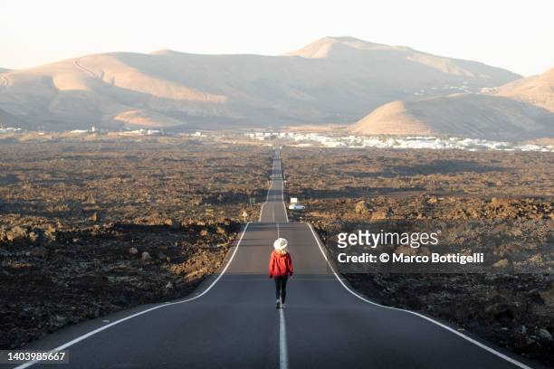 woman walking along a long straight road - lanzarote imagens e fotografias de stock