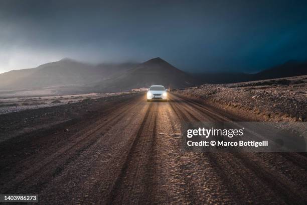 car driving on dirt road at sunset in lanzarote, spain - vehicle light trail stock pictures, royalty-free photos & images