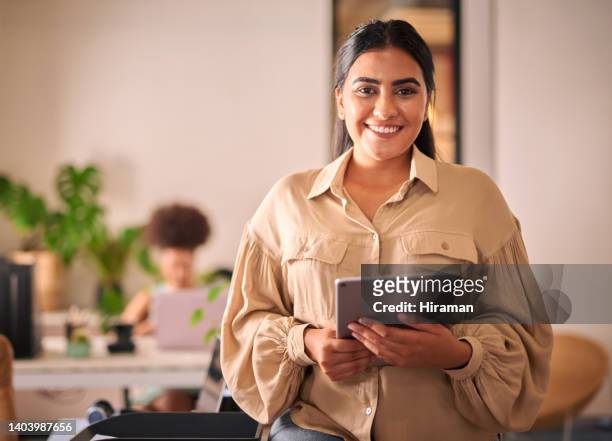 portrait of mixed race businesswoman holding her tablet in the office standing in front of a window. one young female indian developer looking at the camera. innovative entrepreneur design firm - looking to the camera stock pictures, royalty-free photos & images