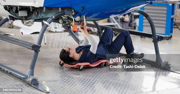 a female aircraft mechanic lies under the helicopter and repairs it in the hangar - jet lag stockfoto's en -beelden