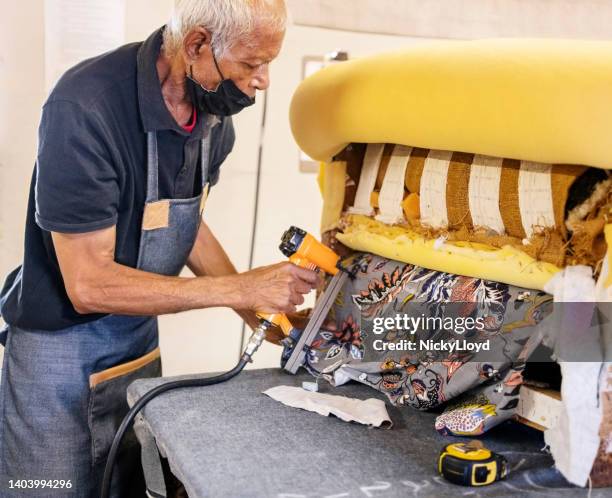 senior upholstery worker fixes the fabric with a pneumatic stapler in the workshop - upholstry stockfoto's en -beelden