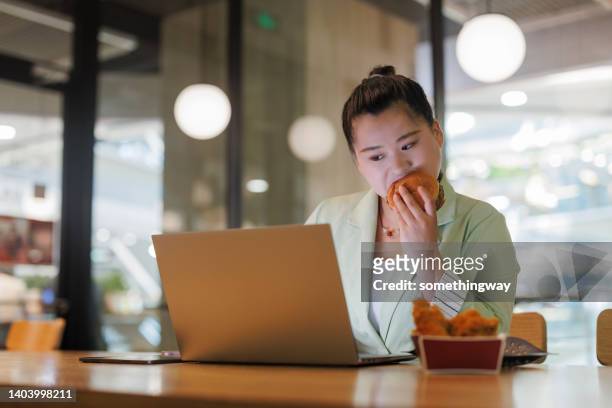 les femmes obèses mangent nerveusement des hamburgers et utilisent des ordinateurs portables dans les restaurants - burger portrait photos et images de collection