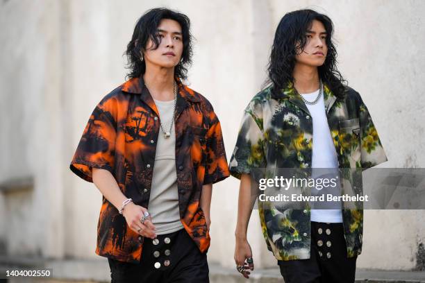 Guest wears silver earrings, a silver chain necklace, a brown and orange tie and dye print pattern short sleeves oversized shirt from Prada, a beige...