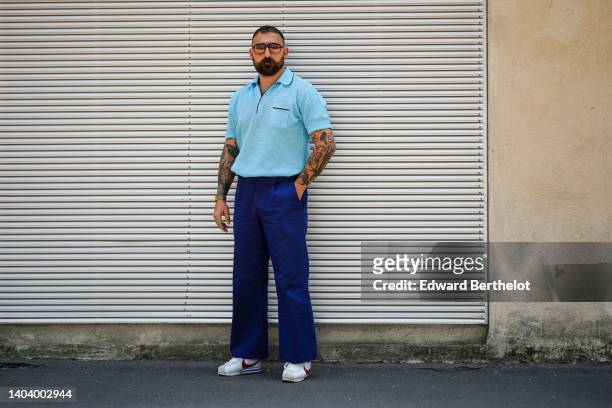 Guest wears sunglasses, a pale blue polo short sleeves shirt, navy blue suit pants, white with burgundy details sneakers from Nike, outside the Prada...