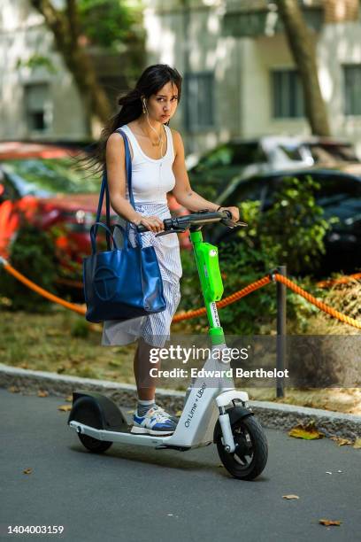 Guest wears gold earrings, a gold chain pendant necklace, a white ribbed tank-top, a royal blue shiny leather oversized Telfar shoulder bag, a white...