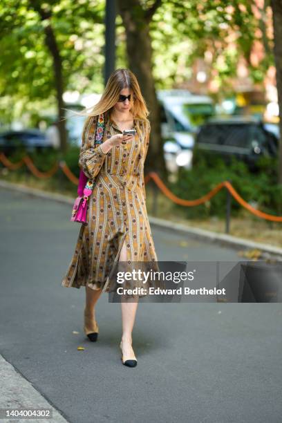 Guest wears black sunglasses, pearl earrings, a gold chain pendant necklace, a brown / orange / black / white print pattern long sleeves / belted /...