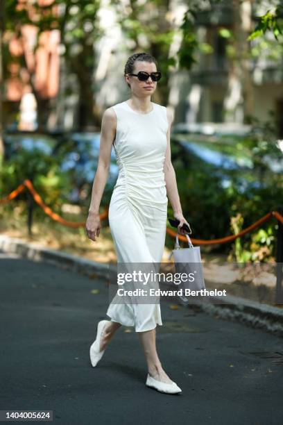 Guest wears black sunglasses, a white tank-top long tube dress, a pale gray matte leather handbag, white leather pointed ballerinas, outside the Etro...