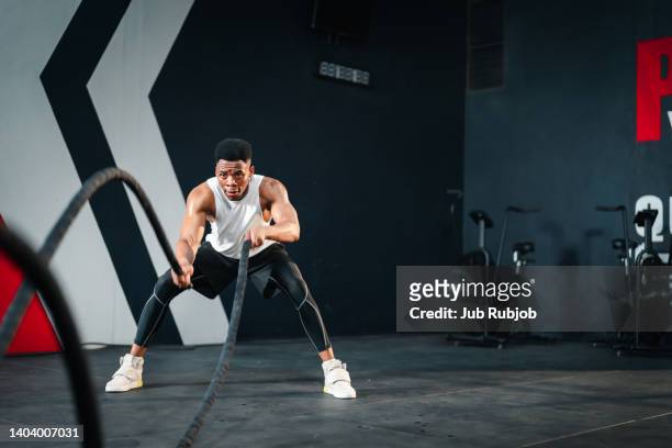african descent man doing battle rope exercise in cross training. - schlachtfeld stock-fotos und bilder