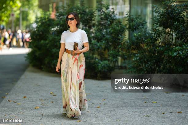Guest wears black sunglasses, a white t-shirt, a camel shiny leather large belt, a white latte with red / green flower print pattern pleated tulle...