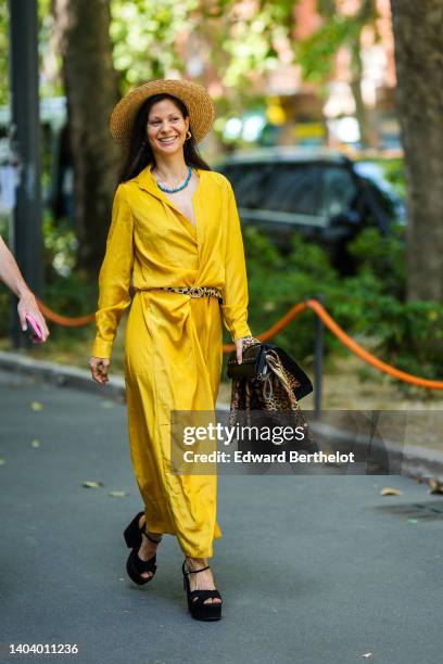 Singer Talitha Imara wears a beige wicker hat, gold earrings, a blue pearls necklace, a yellow long shirt dress, a black with beige print pattern...