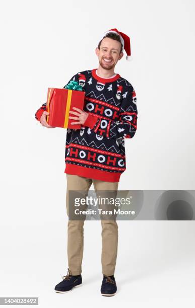 man wearing christmas sweater holding present - suéter natalino - fotografias e filmes do acervo