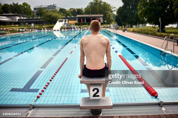 rear view of swimmer sitting on starting block at an outdoor public swimming pool - swimming shorts stock pictures, royalty-free photos & images