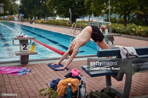 young man practicing yoga at an outdoor public swimming pool - freibad stock-fotos und bilder