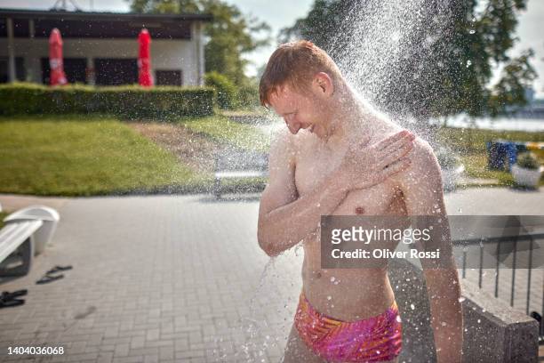 young man taking a shower at an outdoor public swimming pool - bath shower stock pictures, royalty-free photos & images
