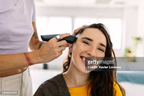 portrait of smiling millennial young woman with his girlfriend shaving hair at home - head shave stockfoto's en -beelden