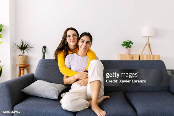 portrait of young female couple hugging each other while relaxing at home - union gay stockfoto's en -beelden