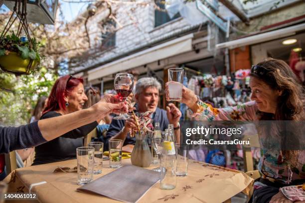 mature friends on a discovery journey over coastal greece enjoying local drinks celebratory toast at a small bar on a street in preveza - saitan bazaar - epirus greece stock pictures, royalty-free photos & images