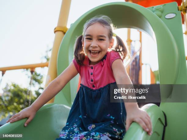 glückliches kleines mädchen, das draußen auf dem spielplatz spielt - rutsche stock-fotos und bilder