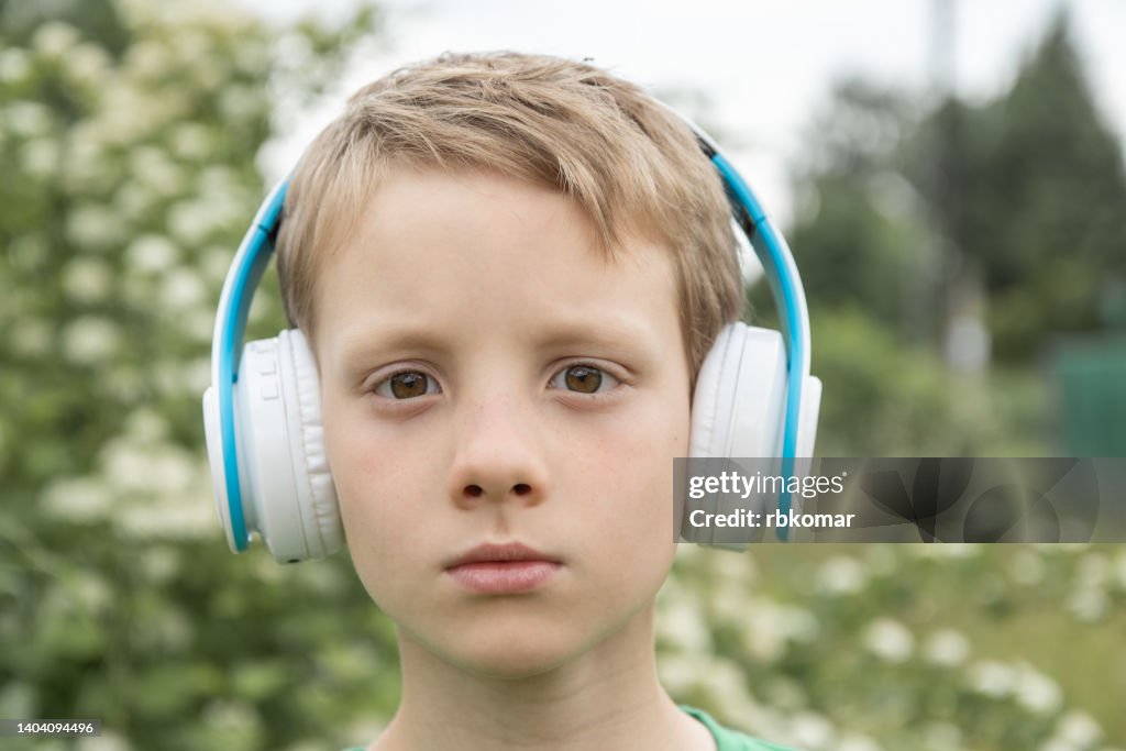 Serious boy 8 years old in bluetooth headphones listening to music in nature