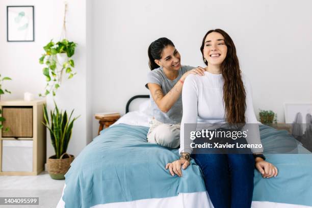 young female couple in love - trendy woman giving his girlfriend a massage on shoulders while sitting on bed - man touching shoulder stock-fotos und bilder