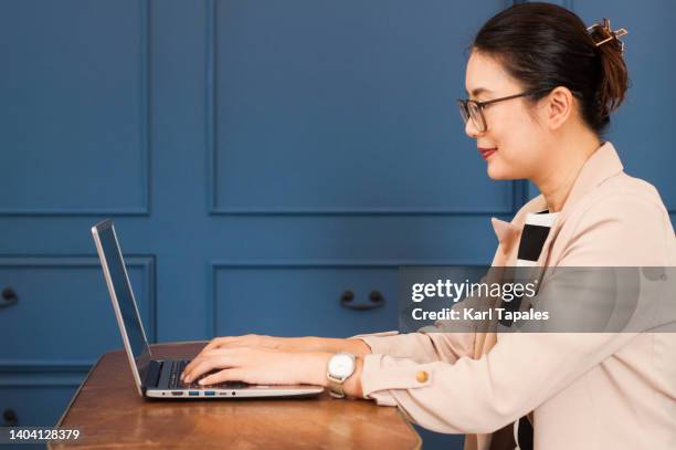 a southeast asian woman is using laptop for virtual work in the office - daily life in philippines stock-fotos und bilder