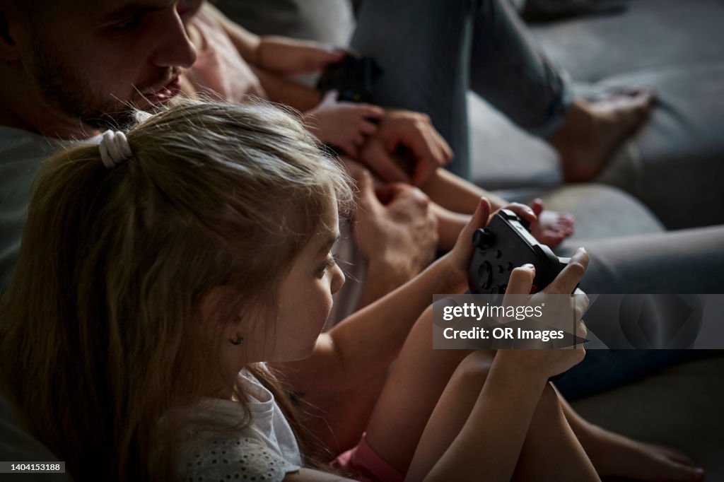 Father with daughter holding game controller at home