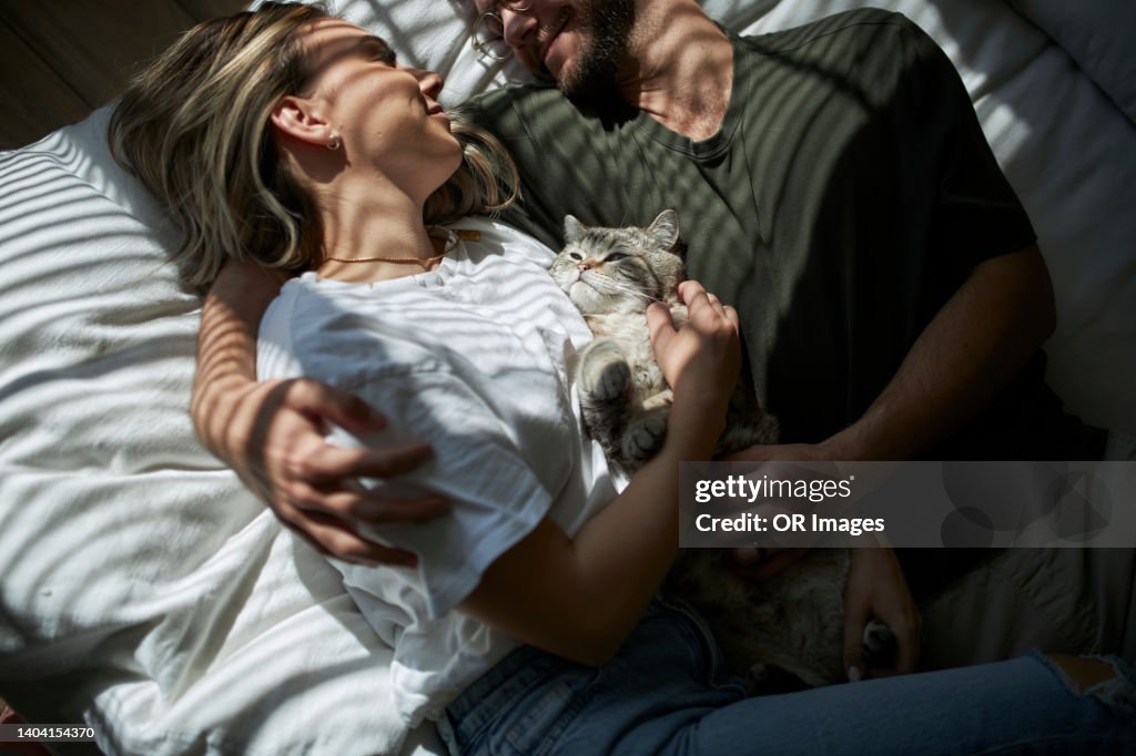 Young couple lying on bed with a cat