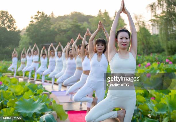 Women practice yoga on a footpath above a lotus pond on June 21, 2022 in Taizhou, Jiangsu Province of China. The International Day of Yoga is...