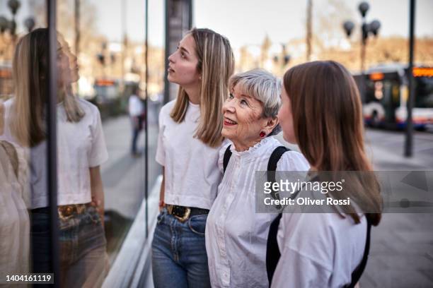 senior woman  and two young women looking in shop window in the city - shopping friends family stock pictures, royalty-free photos & images