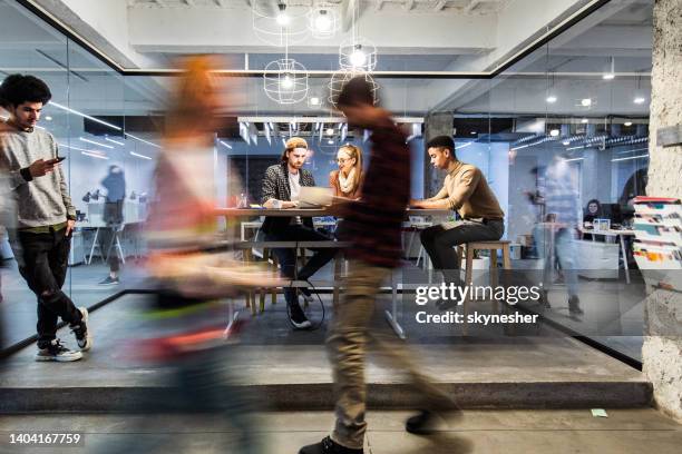 junge kreative, die im büro unter menschen in verschwommener bewegung arbeiten. - promotion stock-fotos und bilder