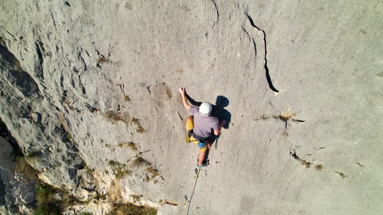 Detaching Rope AERIAL: Young male climber attaching the rope with quickdraw while lead ...
