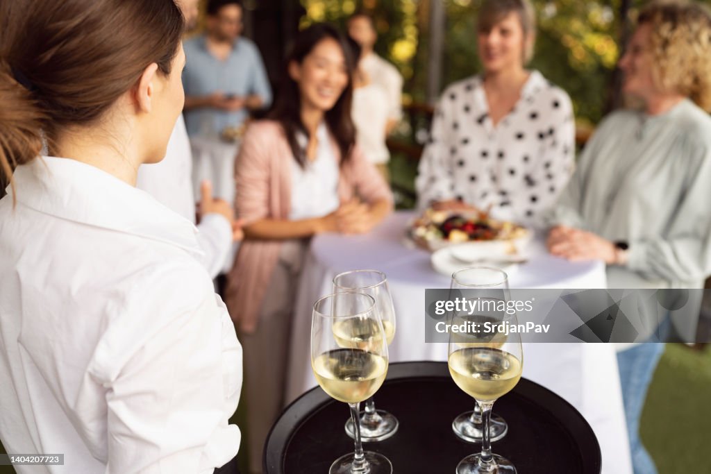 Unrecognizable waitress carrying tray with glasses of white wine, during banquet