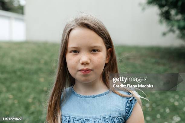 a schoolgirl girl with long blond hair and wide-open brown eyes looks at the camera with a serious look on the street - young face serious at camera photos et images de collection