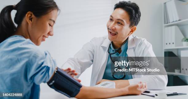 成熟したアジア人男性の医師は、診療所で女性患者の高低血圧を測定します。 - high blood pressure ストックフォトと画像