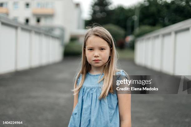 a schoolgirl girl with long blond hair and wide-open brown eyes looks at the camera with a serious look on the street - blonde hair brown eyes stock pictures, royalty-free photos & images