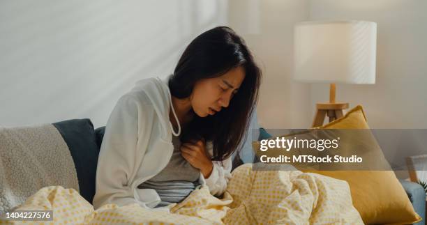 sick young asian woman having heart attack sitting on sofa in living room at home. - chest pain stock pictures, royalty-free photos & images