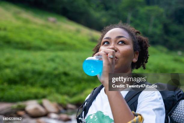 young black woman drinking electrolyte drink after hiking on the mountain - electrolyte stock pictures, royalty-free photos & images