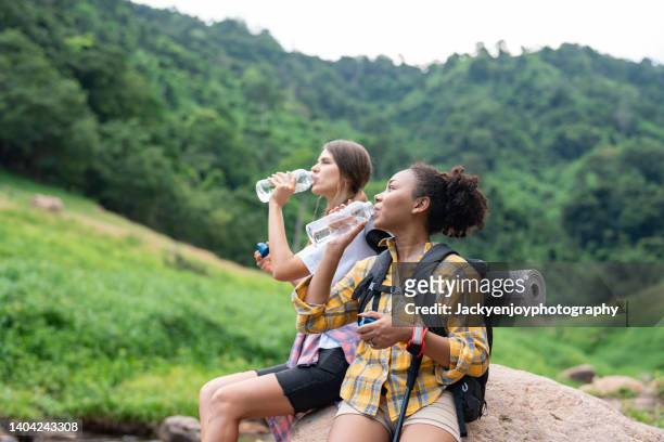 two young women walking through the jungle taking a break and drinking water from bottles - hiking australia stock pictures, royalty-free photos & images